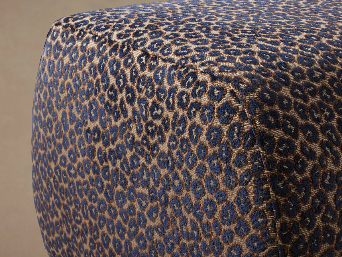 Fresno Ottoman, blue and tan leopard print rectangular ottoman with rounded edges, on a wooden floor against a beige wall.