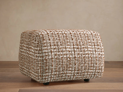 Front view of a Fresno Ottoman featuring a beige, brown, and gray woven checkered pattern, on a patterned rug.