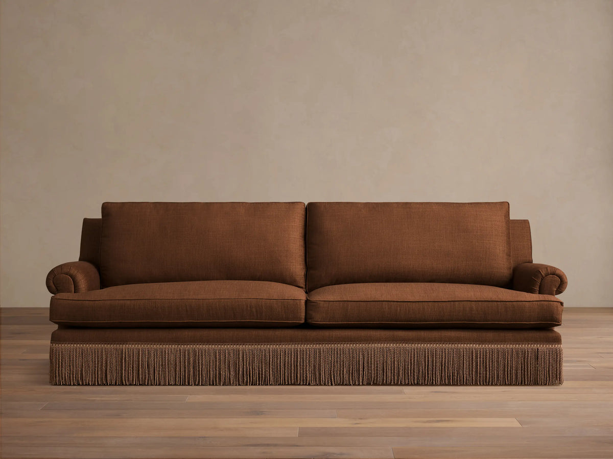 Front view of the brown McKinley Sofa with Fringe, featuring rolled arms, plush cushions, and a distinctive fringe along the base.