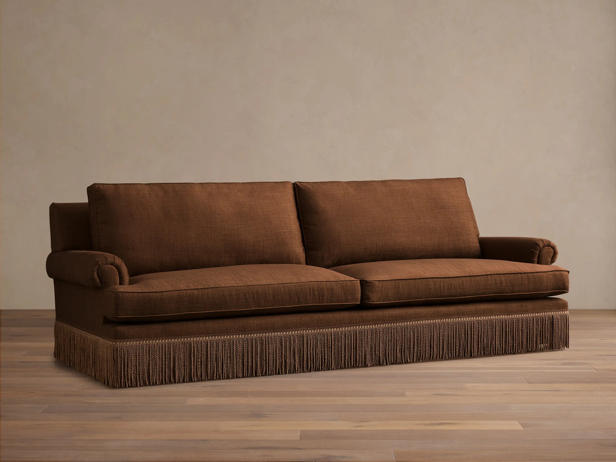 Front view of a brown McKinley Sofa with Fringe, featuring two seat cushions, rolled arms, and detailed brown fringe along the base.