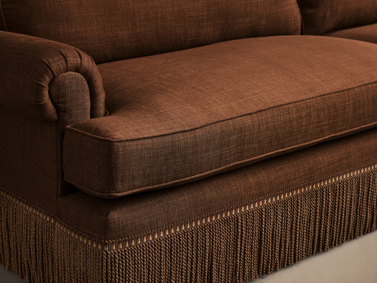Close-up of Brown McKinley Sofa with Fringe, showing a rolled arm, plush seat cushion, and braided tassel fringe along the base.