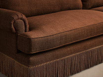 Close-up of Brown McKinley Sofa with Fringe, showing a rolled arm, plush seat cushion, and braided tassel fringe along the base.