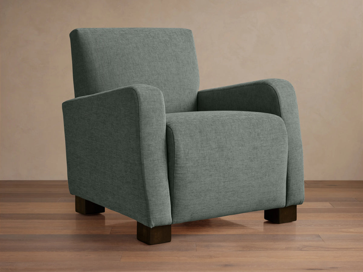 Upholstered Kershaw Chair in soft green fabric, featuring a boxy design with plush, straight arms and dark wooden legs on a wooden floor.