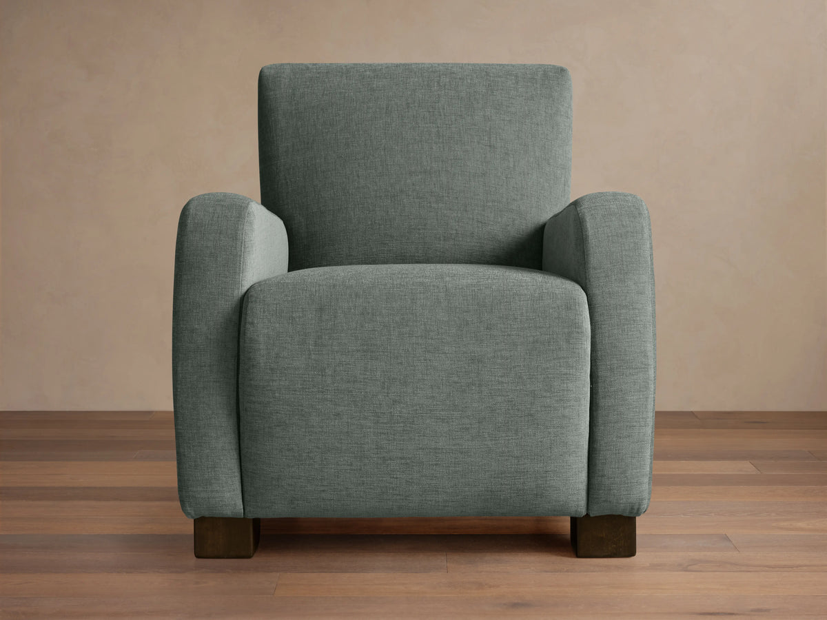Upholstered Kershaw Chair in soft green fabric, featuring a boxy design with plush, straight arms and dark wooden legs on a wooden floor.