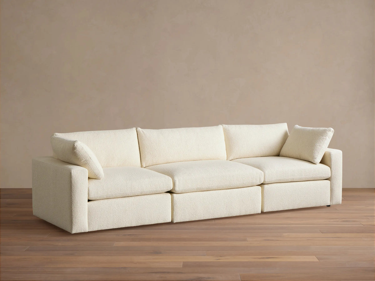 Beale Three-Piece Modular Sofa in cream textured fabric, with two accent pillows. Full frontal view on wood floor.
