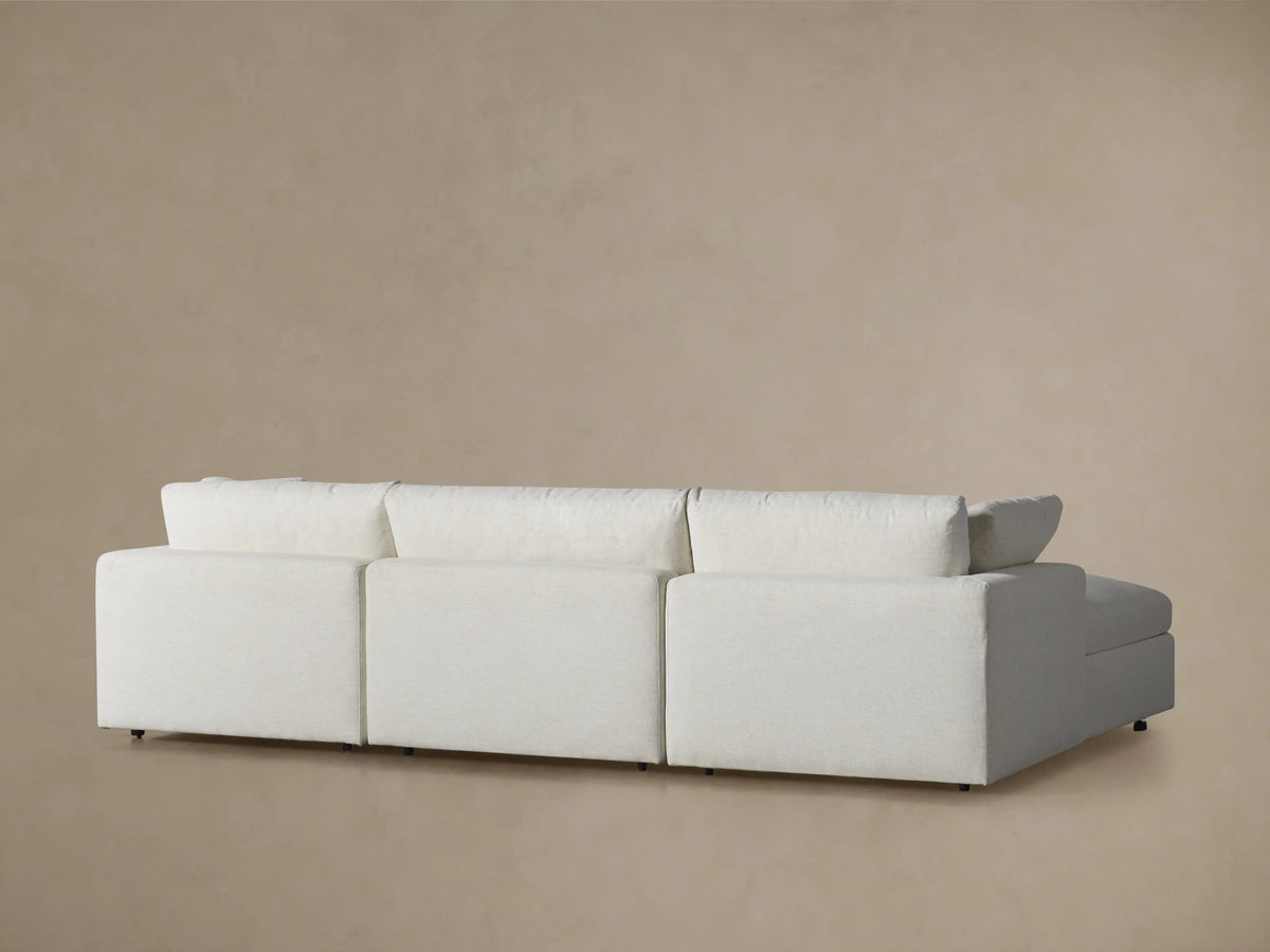 Beale Four-Piece Sectional close-up. Light gray textured fabric armrest and soft back cushion with a slight wrinkle, beige wall.
