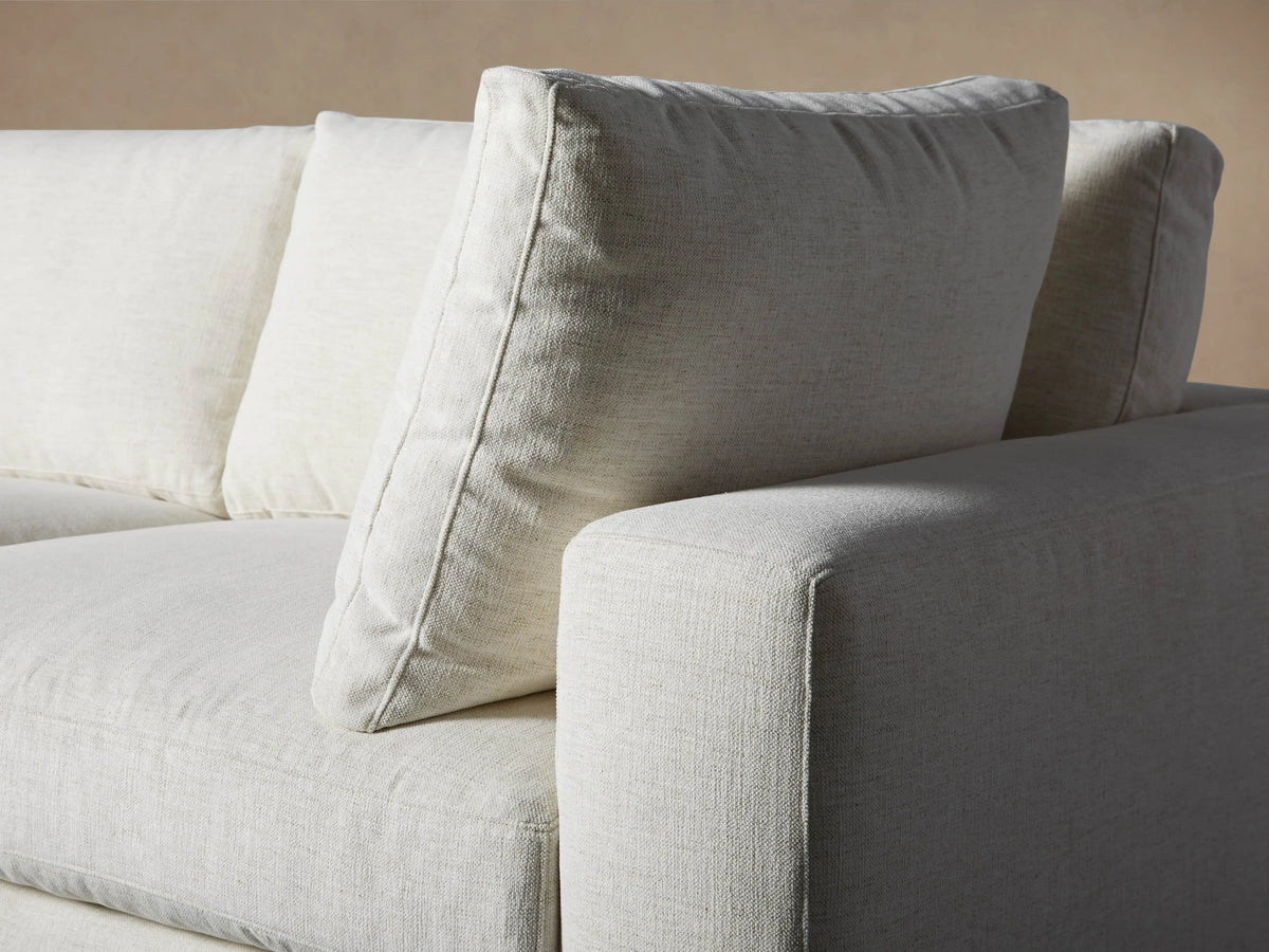 Beale Five Piece Sectional sofa, light cream L-shape with plush cushions and ottoman, against a beige wall on wood floor.