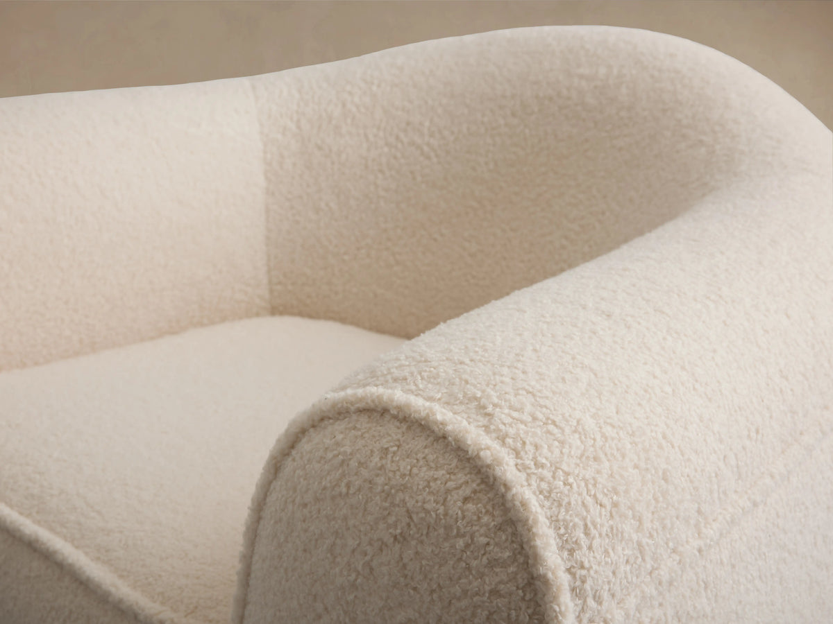 Barret Chair in cream fabric with rounded armrests and a cushioned seat on a wood floor, featuring a smooth, curved back.