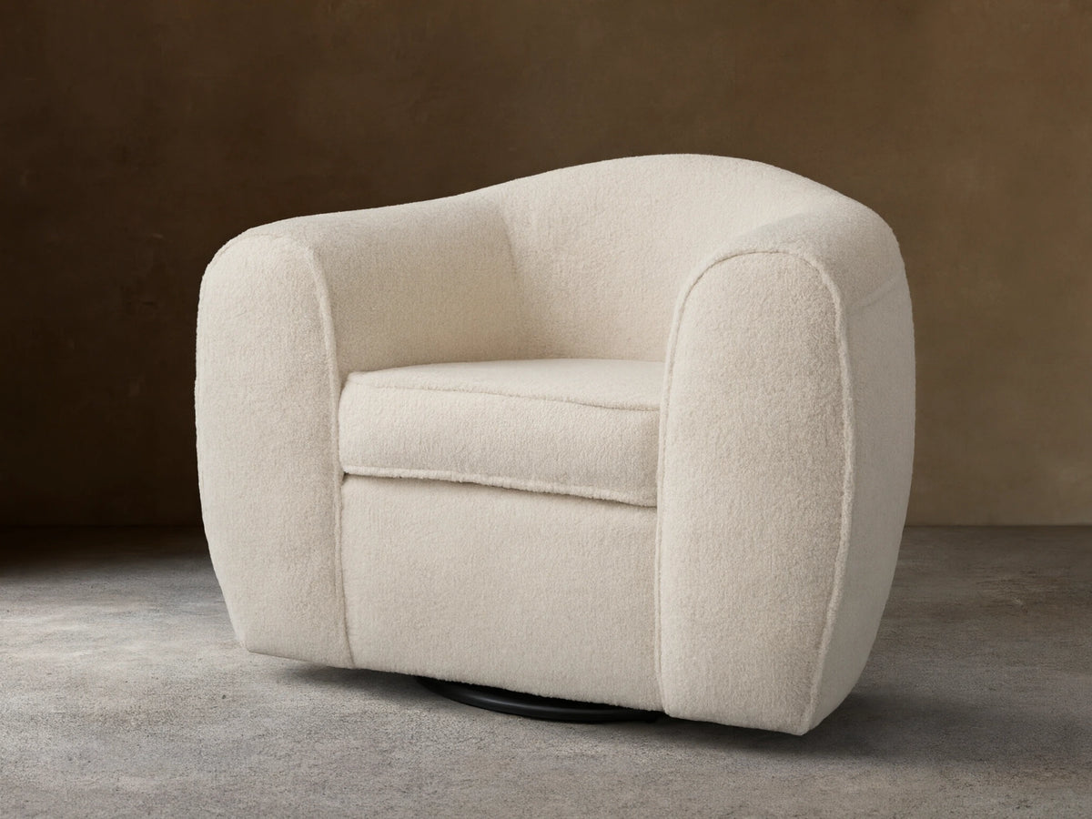 Cream-colored Barret Chair with plush, rounded armrests and backrest. Features a soft fabric texture and a solid base for swivel rotation.