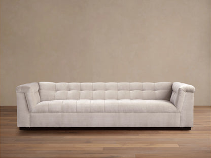 Cameran Sofa in beige fabric with tufted backrest and low armrests, set on a wood floor against a beige wall.