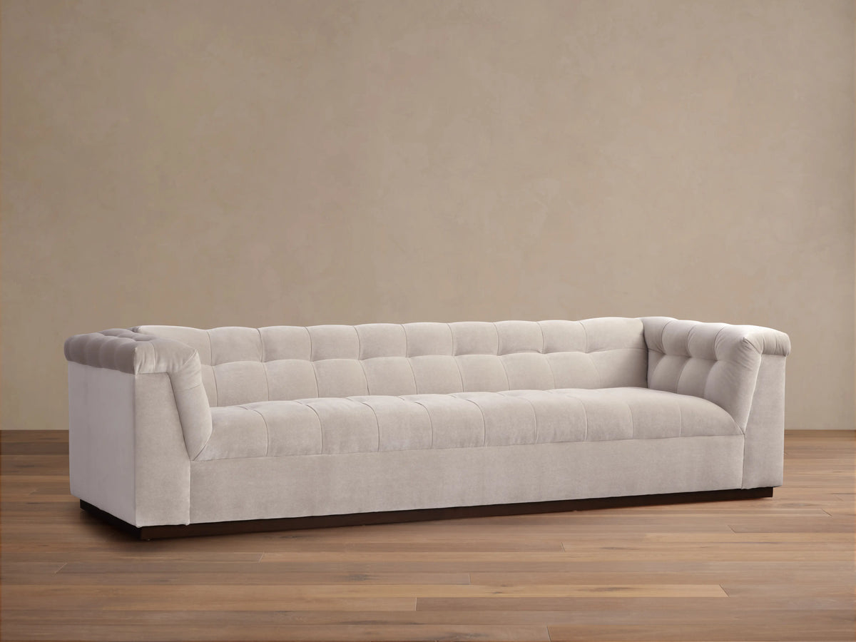 Cameran Sofa in beige fabric with tufted backrest and low armrests, set on a wood floor against a beige wall.