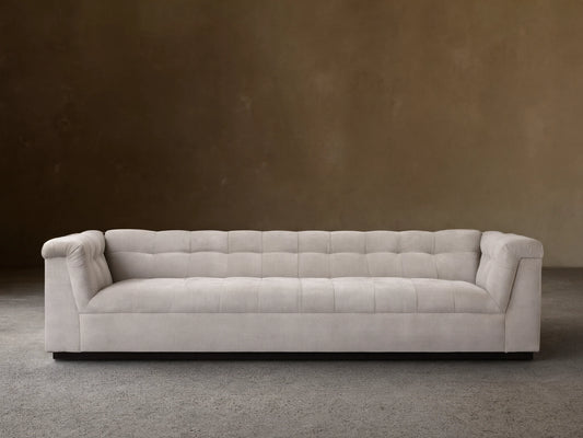 Cameran Sofa in beige fabric with tufted backrest and low armrests, set on a wood floor against a beige wall.