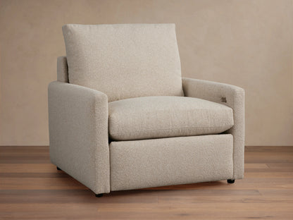 Kipton Motion Recliner in light beige fabric with slim rectangular arms, plush seat, and back cushion on a wooden floor.