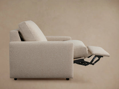 Kipton Motion Recliner close-up shows beige fabric texture, slim armrest with metal button for reclining, and cushion detail.