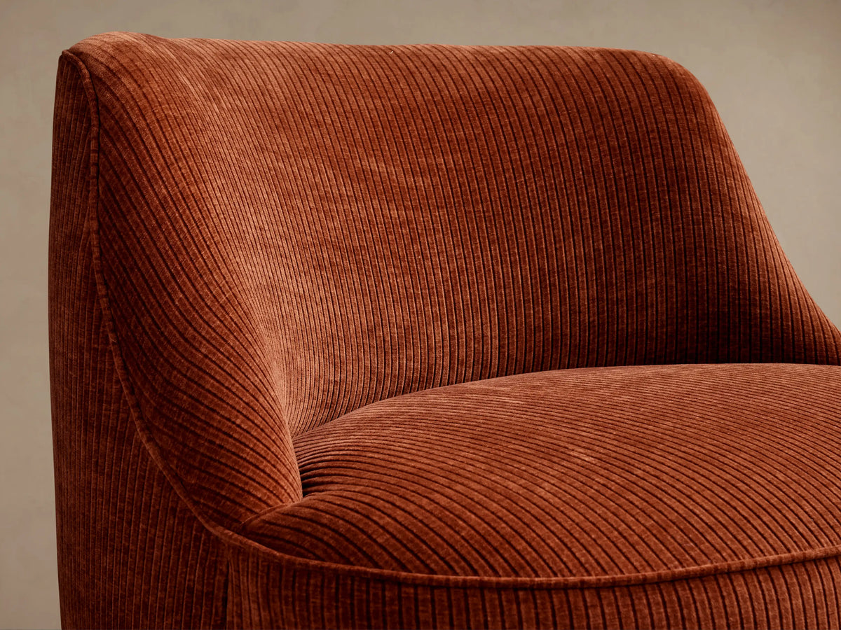 Sonny Swivel Chair, rust orange corduroy, armless with a curved back and round base, on a wood floor in a neutral room.