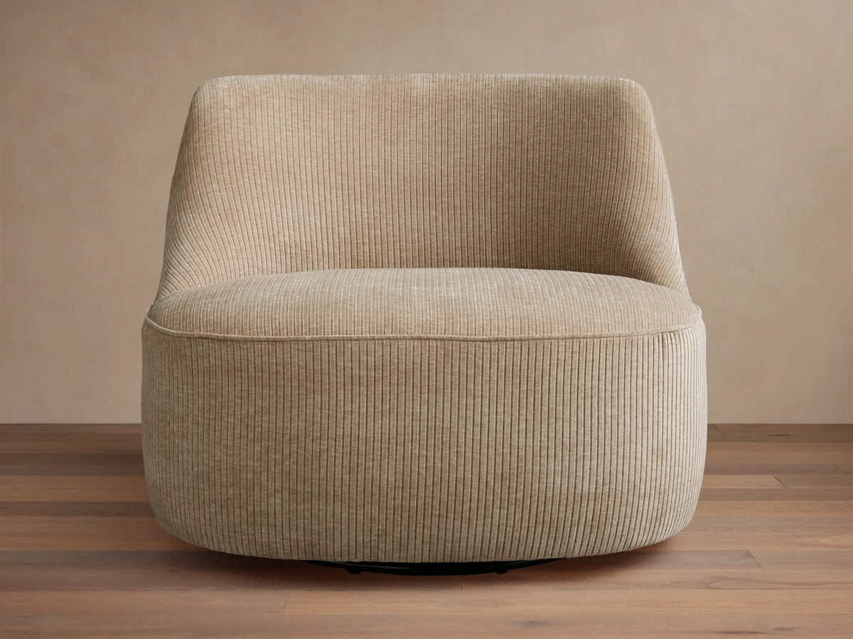 Sonny Swivel Chair, upholstered in light beige ribbed fabric, slightly angled on a wooden floor against a light wall.