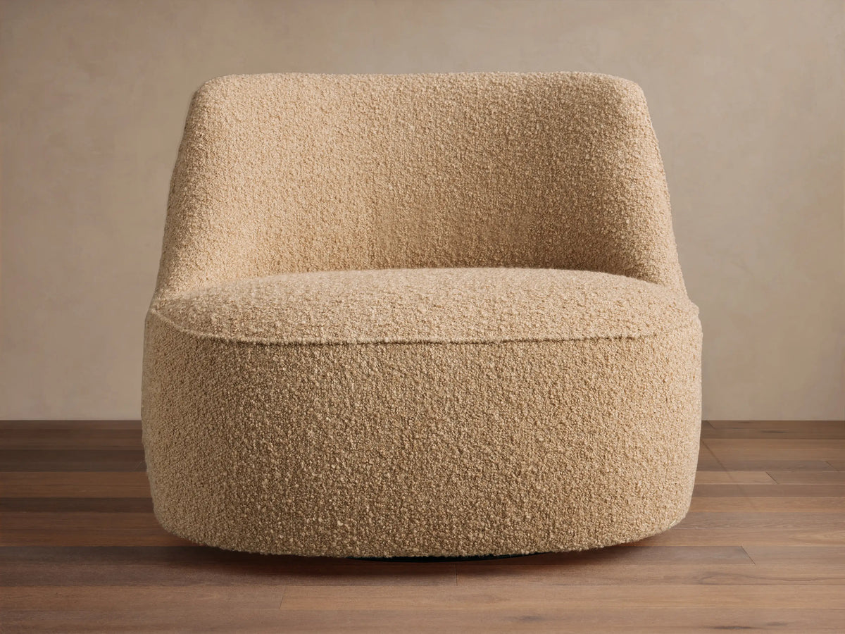 Sonny Swivel Chair, rounded, armless, light beige bouclé fabric, on wood floor against a neutral wall.