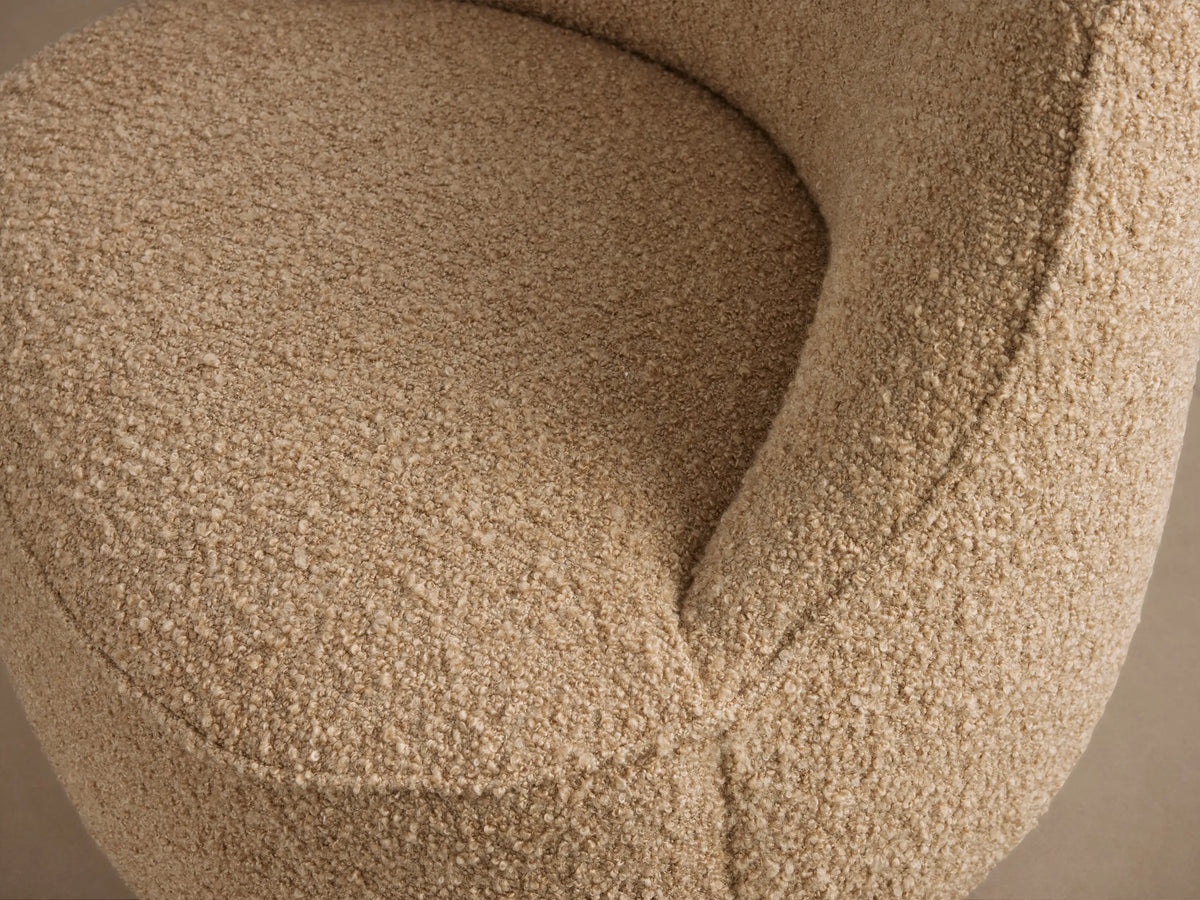 Sonny Swivel Chair, upholstered in textured light beige fabric, with a round base and curved back, on a wooden floor.