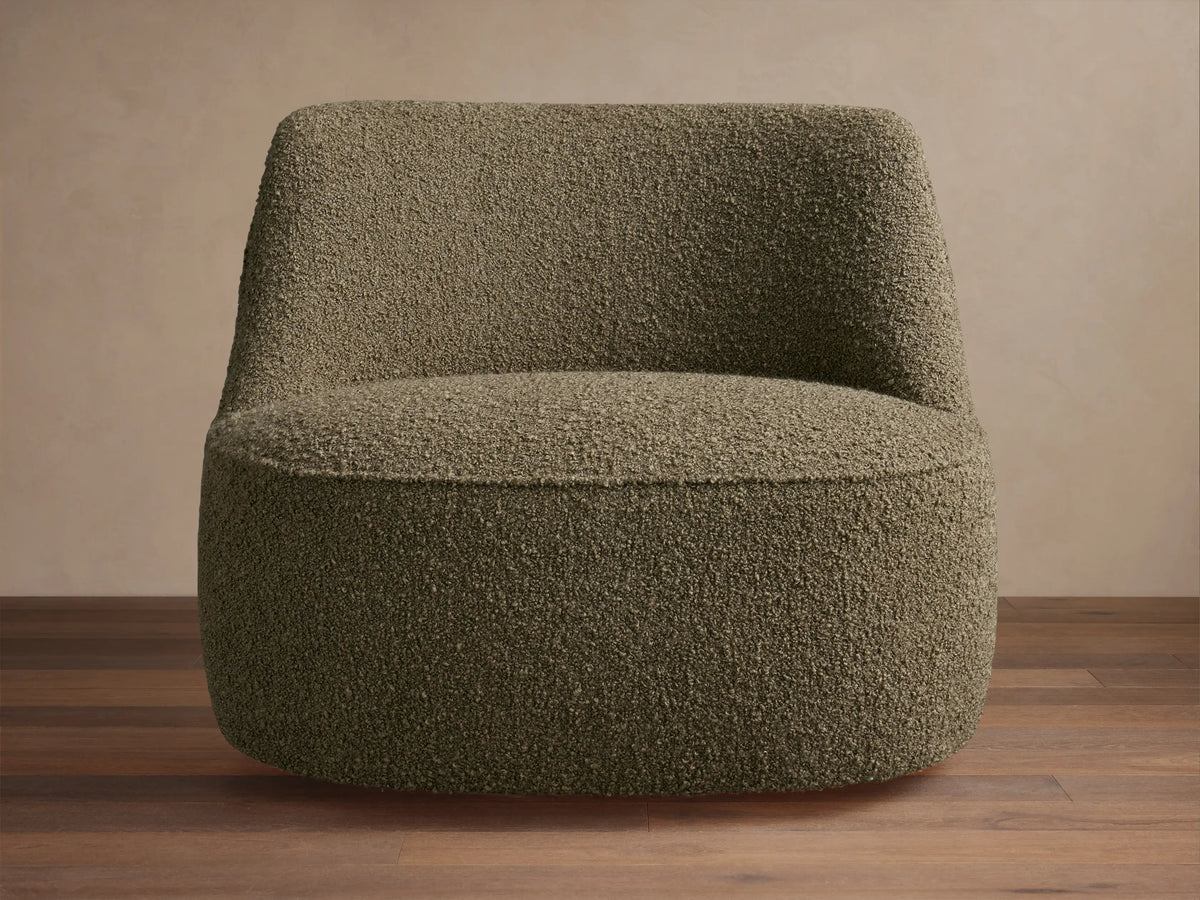 Textured olive green Sonny Swivel Chair, armless with a curved back & wide round base, sitting on a wooden floor.