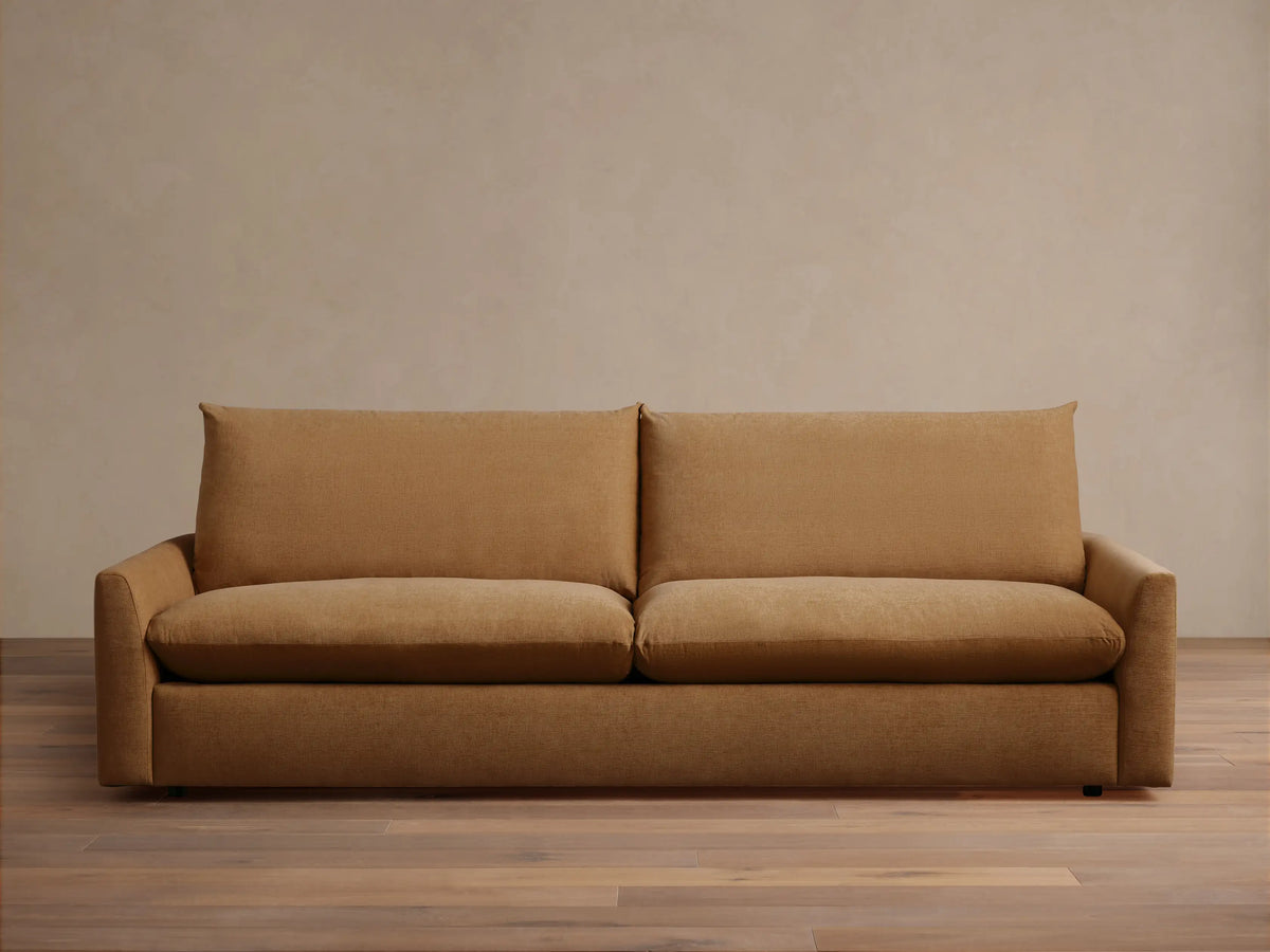 Calistoga Sofa in warm brown fabric, plush backrests and wide seat cushions on sleek wooden flooring against a beige wall.
