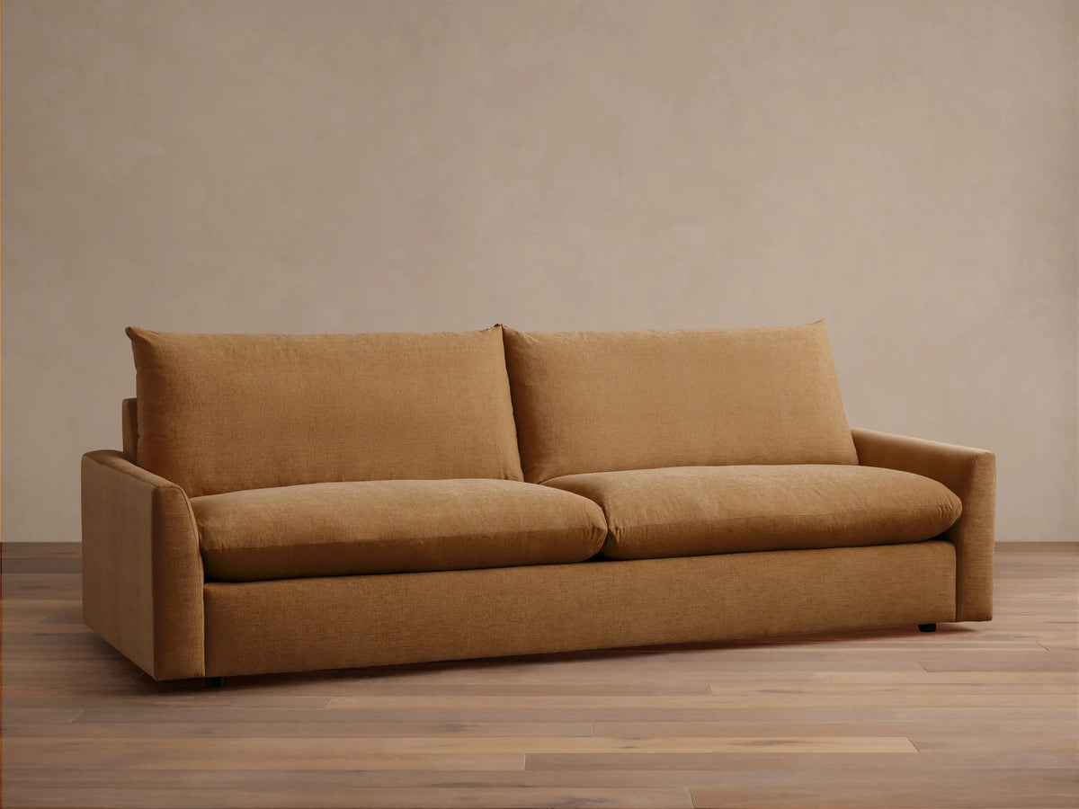 Calistoga Sofa in warm brown fabric, plush backrests and wide seat cushions on sleek wooden flooring against a beige wall.