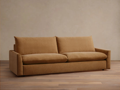 Calistoga Sofa in warm brown fabric, plush backrests and wide seat cushions on sleek wooden flooring against a beige wall.