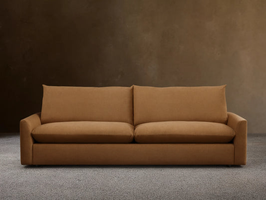 Calistoga Sofa in warm brown fabric, plush backrests and wide seat cushions on sleek wooden flooring against a beige wall.