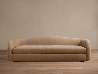 Ashlyn Sofa in warm tan, front view. Modern, minimalist design with a gently curved backrest and integrated arms on a wooden floor.