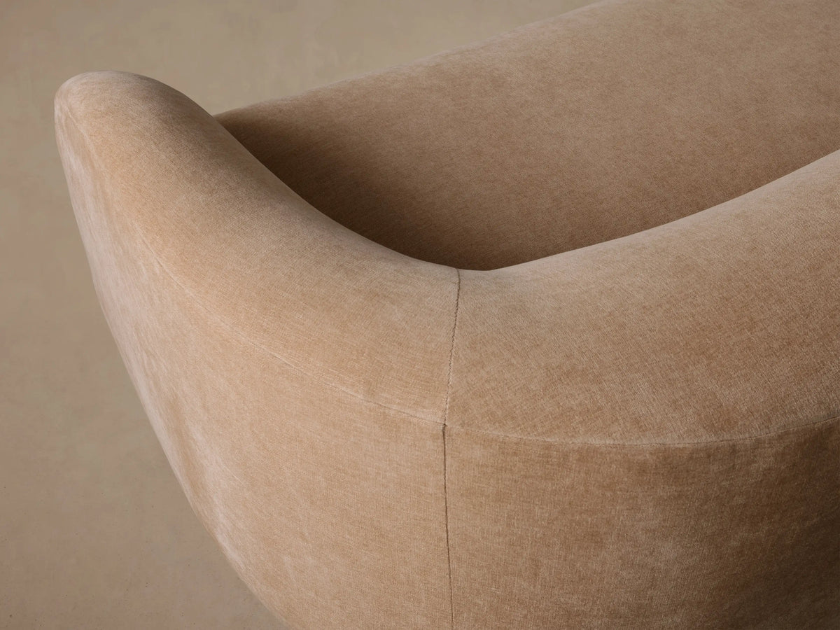 Ashlyn Sofa, a light beige curved sofa with rounded arms, on a wooden floor against a neutral background.