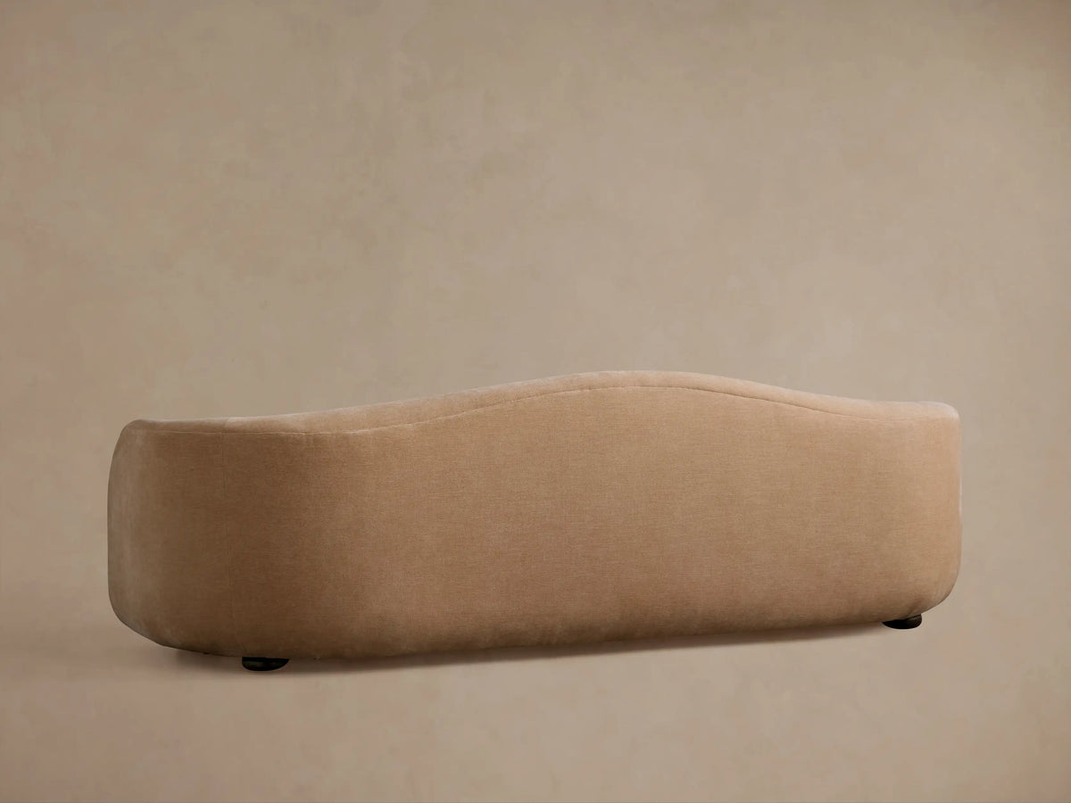 Close-up of Ashlyn Sofa's curved back & armrest, soft warm beige textured fabric, subtle vertical seam.