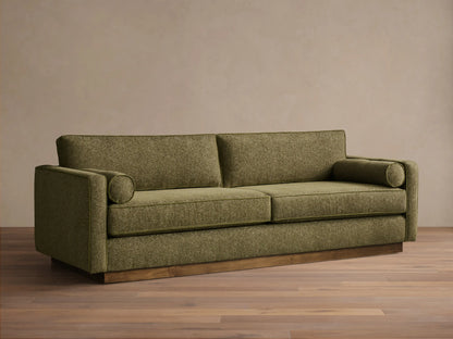 Front view of the Plush Olive Munroe Sofa, featuring two cylindrical arm pillows and a contrasting wooden base.