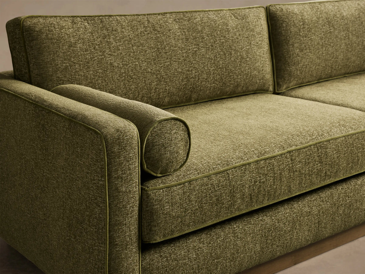 Front view of the Plush Olive Munroe Sofa, featuring two seat and back cushions, bolster pillows, contrast welting, recessed wooden base.