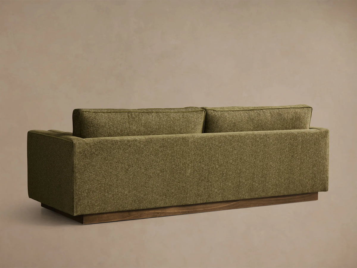 Close-up of the Plush Olive Munroe Sofa, showing the textured fabric, detailed light green welting, and armrest with bolster.