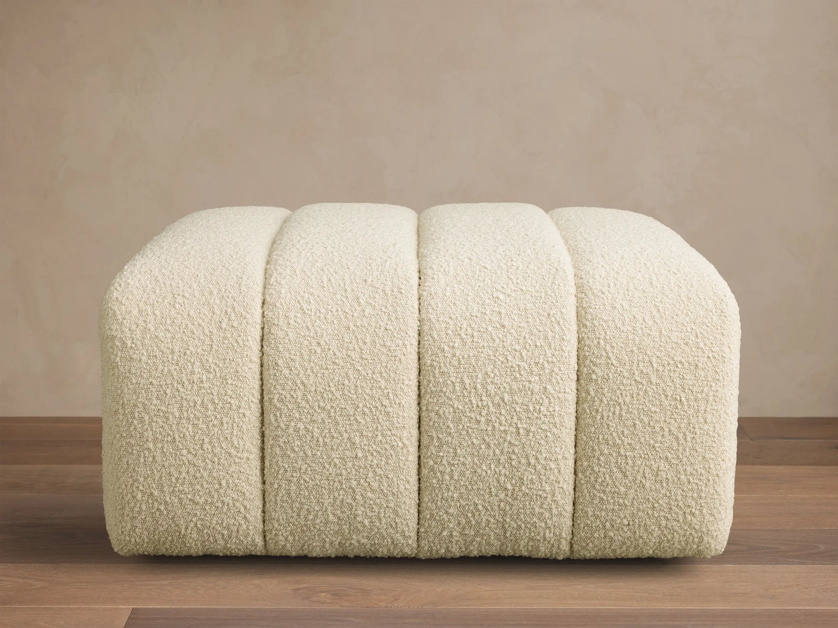 Front view of a cream channel-tufted Bracco Ottoman with rounded edges, upholstered in bouclv© fabric.