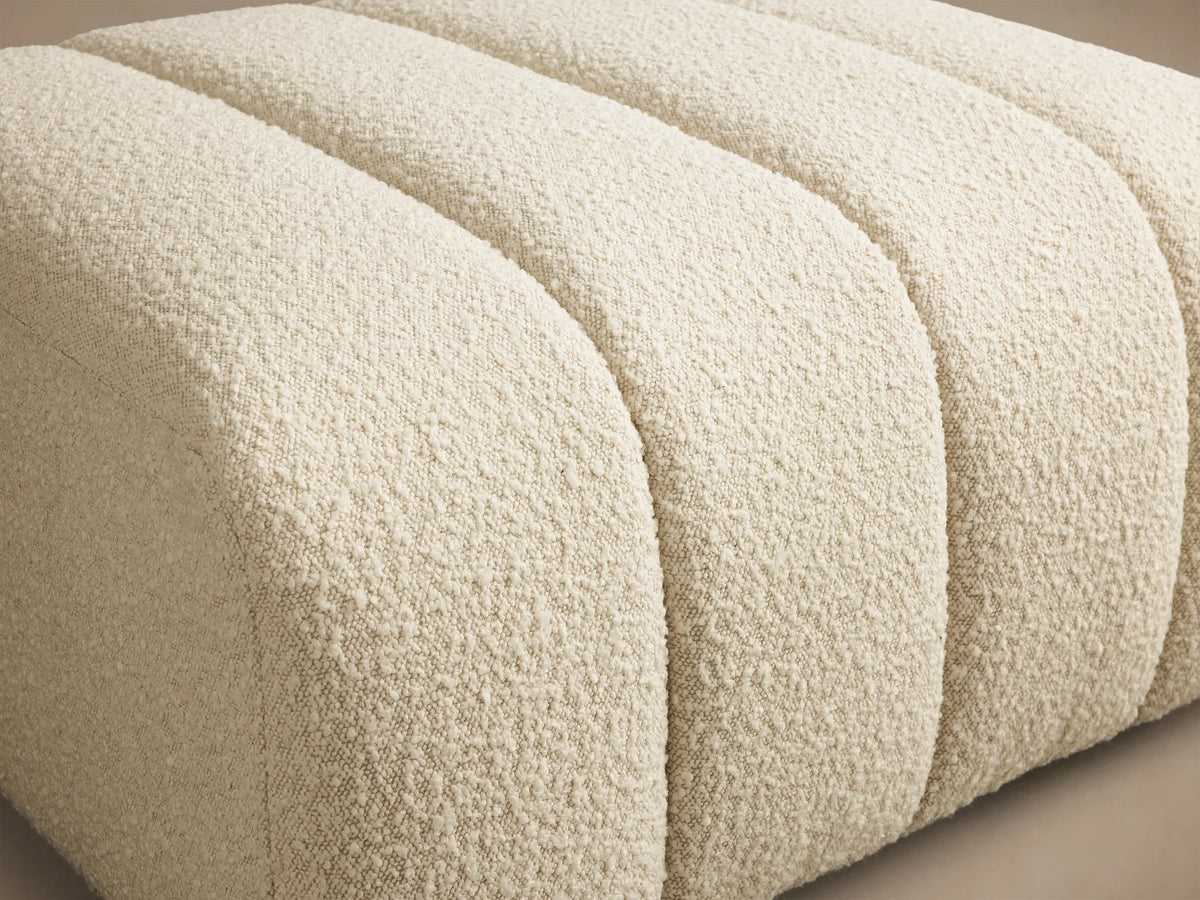 Close-up of the cream textured fabric of the Bracco Ottoman, showing its vertical channel tufting.
