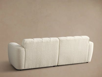 Close-up of the cream Bracco Two-Piece Sofa, featuring textured fabric, vertical channel tufting, and a curved armrest.