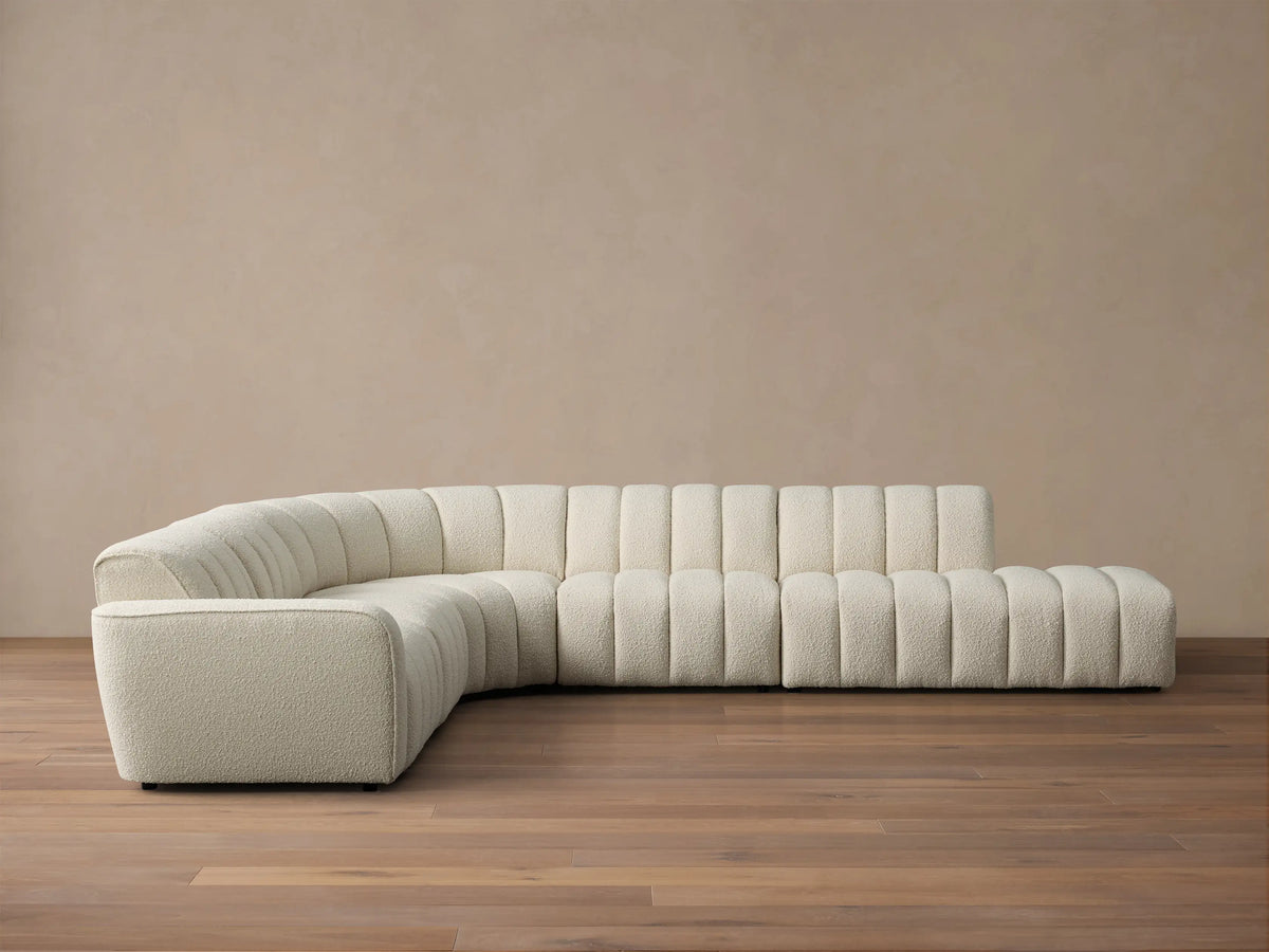 Front view of Cream Bracco Five-Piece Bumper Sectional with channel tufting, curved, on a wooden floor.