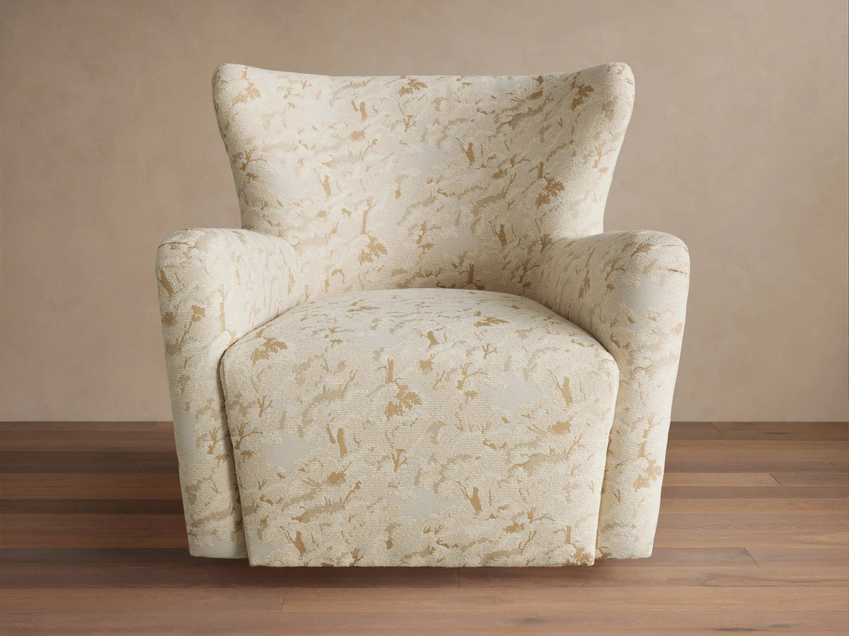 Sasha Swivel Chair, cream with gold abstract pattern, high back, rounded arms, angled left on wood floor.