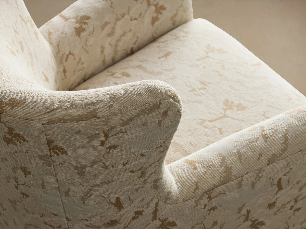 Sasha Swivel Chair, upholstered in cream fabric with a subtle golden-tan abstract pattern, front view against a wall.