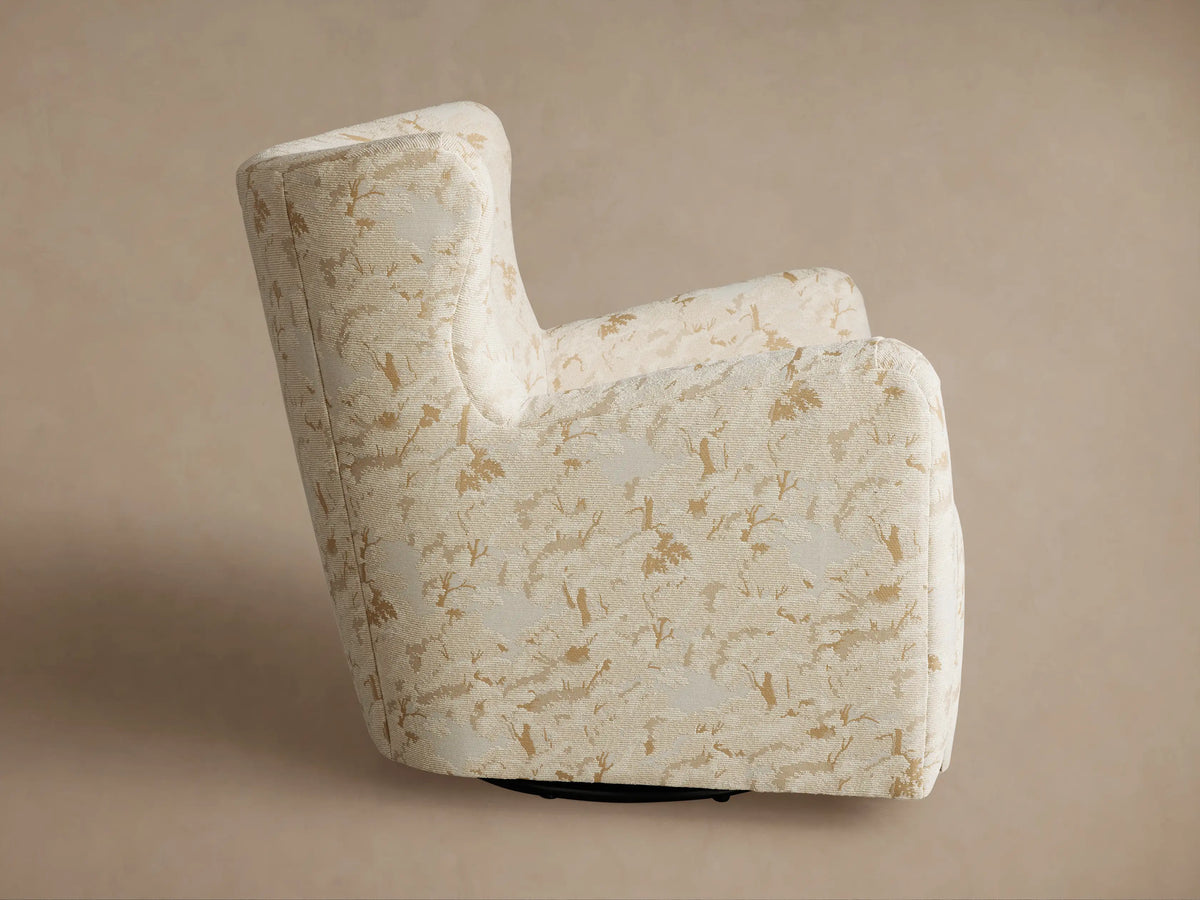 Sasha Swivel Chair with cream fabric & gold botanical pattern, viewed from back-left. Dark swivel base visible.