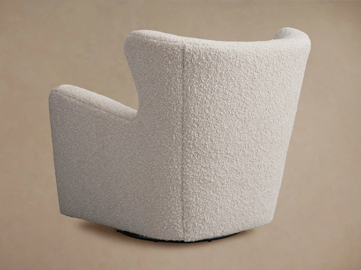 Sasha Swivel Chair in textured, cream-colored fabric, side view showing curved backrest and seat, on a solid base.