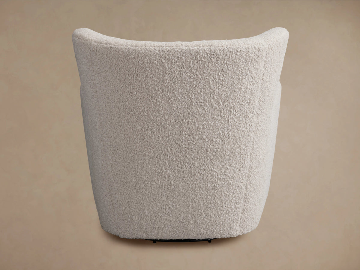 Sasha Swivel Chair in beige textured fabric, angled view. Curved backrest, visible seam, and black swivel base.