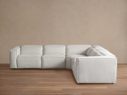 Light cream Coburn Five-Piece Motion Corner Sectional on a wooden floor, against a tan wall.