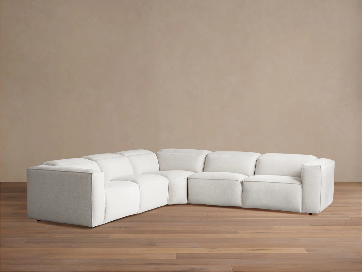 Light cream Coburn Five-Piece Motion Corner Sectional on a wooden floor, against a tan wall.