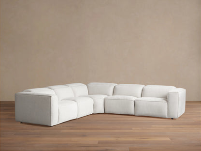 Light cream Coburn Five-Piece Motion Corner Sectional on a wooden floor, against a tan wall.