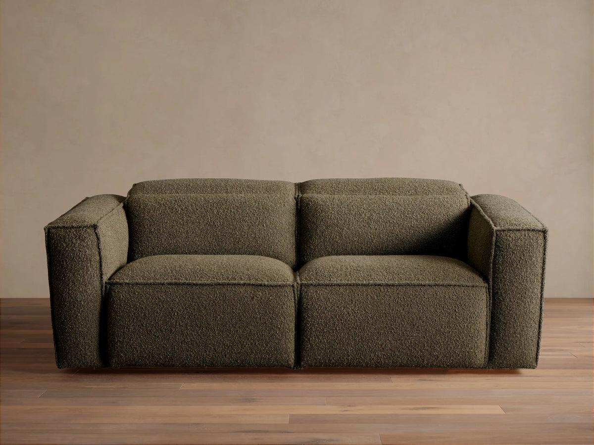 Coburn Two-Piece Motion Sofa in dark olive green textured fabric, a modern two-seater with square arms, on a wood floor.