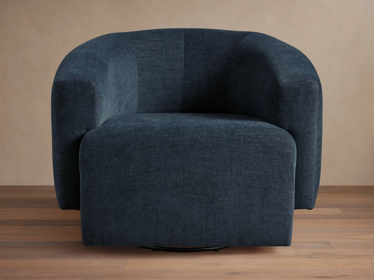 Dark blue Hamlin Swivel Chair on wooden floor, featuring a rounded backrest and armrests. Chair has a solid steel swivel base.