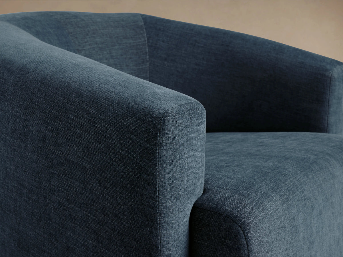 Dark blue Hamlin Swivel Chair on wooden floor, featuring a curved backrest and wide seat with a smooth, textured fabric.
