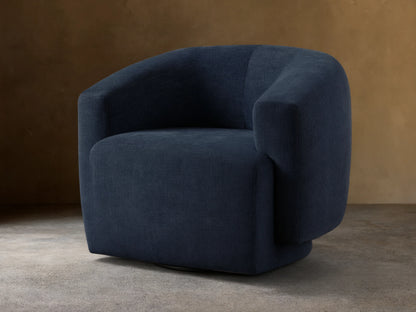 Dark blue Hamlin Swivel Chair on wooden floor, featuring a rounded backrest and armrests. Chair has a solid steel swivel base.