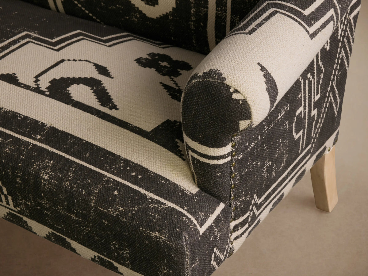 Anya Settee, distressed black and beige tribal patterned upholstery, rolled arms, light wood turned and straight legs, angled right.